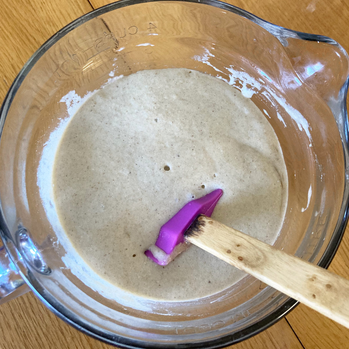 Sourdough waffle batter in a glass measuring cup with a spatula