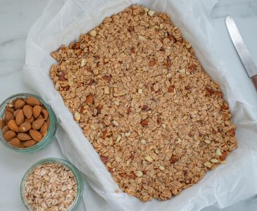 Healthy granola bars in 9x13 pan next to glass bowls of almonds and oats.