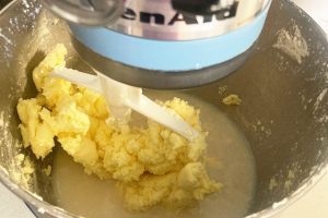 Homemade butter stuck to stand-up mixer paddle with buttermilk in bowl.
