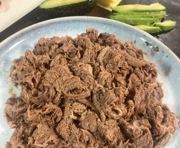 Beef tongue taco meat on a blue plate with avocado and cheese in the background