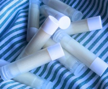 Nine tubes of DIY lip balm scattered on a green and white striped towel