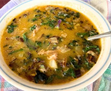 bowl of lamb curry soup in a white bowl with a blue rim and a spoon on a green and pink plaid towel