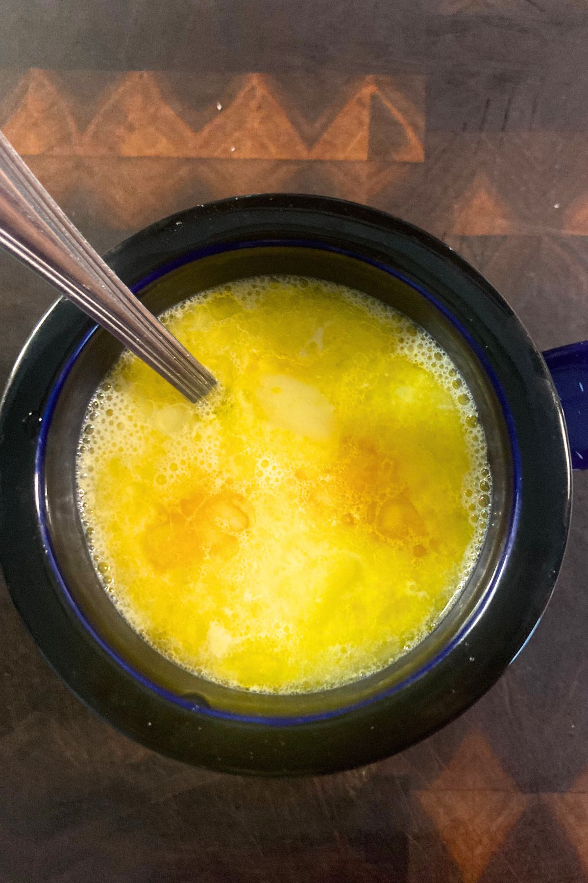 a warm winter drink which is an egg yolk latte or yolky latte in a navy blue and black mug on a wooden cutting board