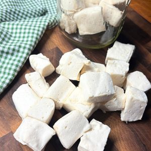 homemade marshmallow on a wooden cutting board in front of a mason jar of marshmallows next to a green and white checked towel