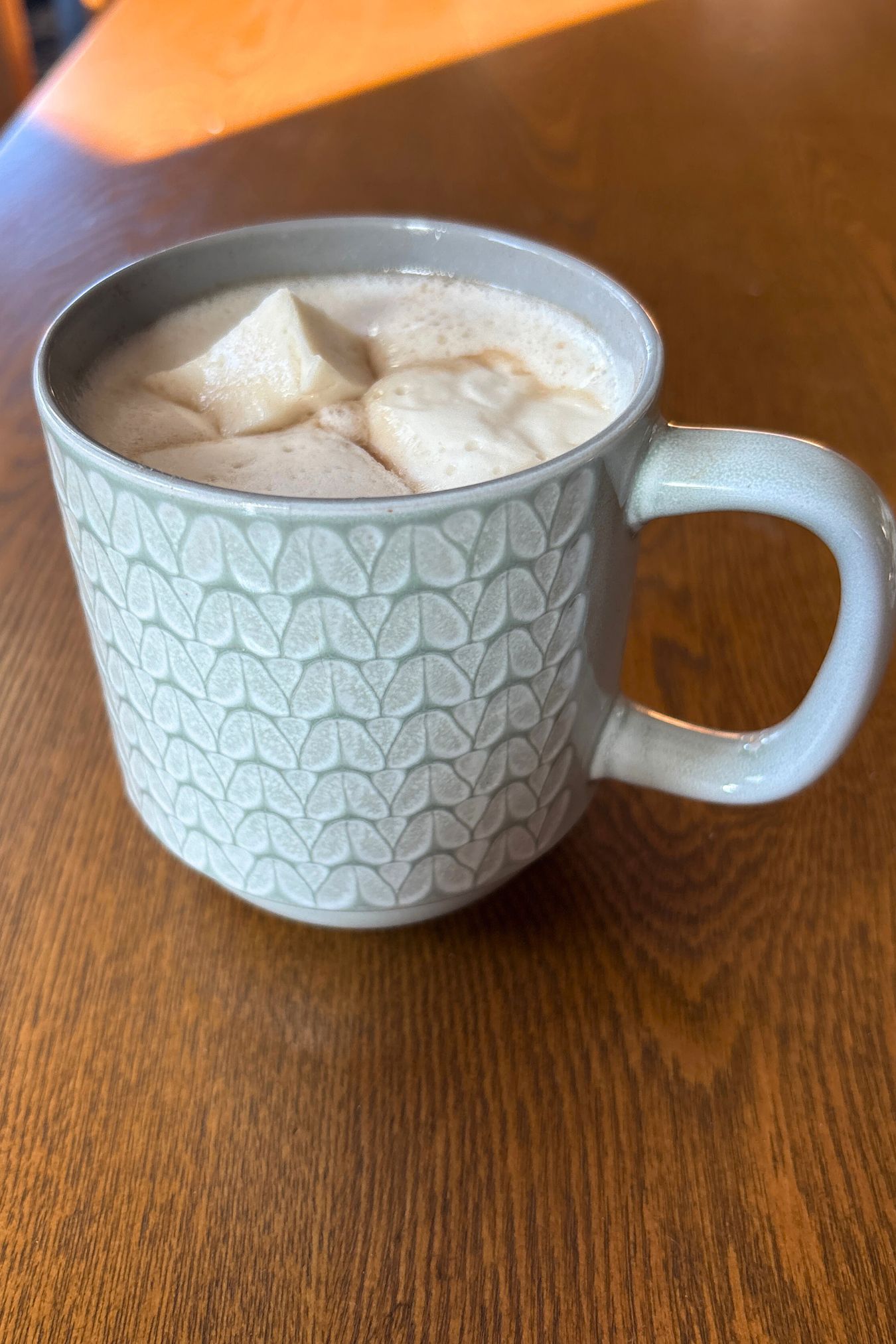 three homemade marshmallow on top of a grey and white mug of hot cocoa on a wooden table