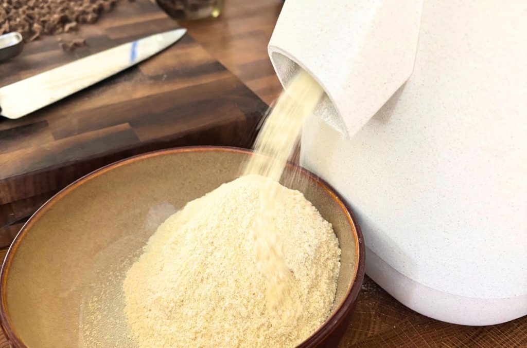 fresh milled flour coming out of a grain mill with a cutting board and knife in background