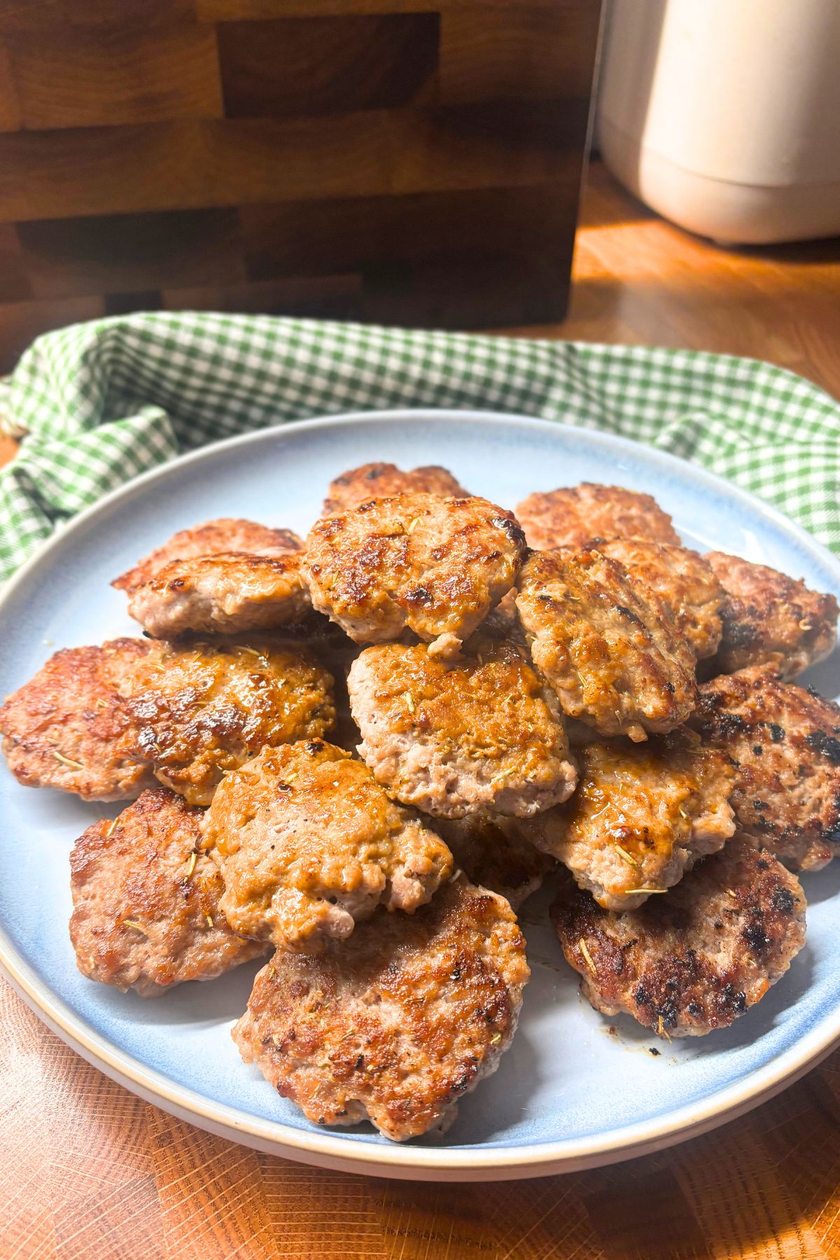 homemade pork breakfast sausage patties on a blue plate with a green gingham towel and cutting board in the background