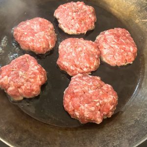 homemade pork breakfast sausage patties frying in a carbon steel pan