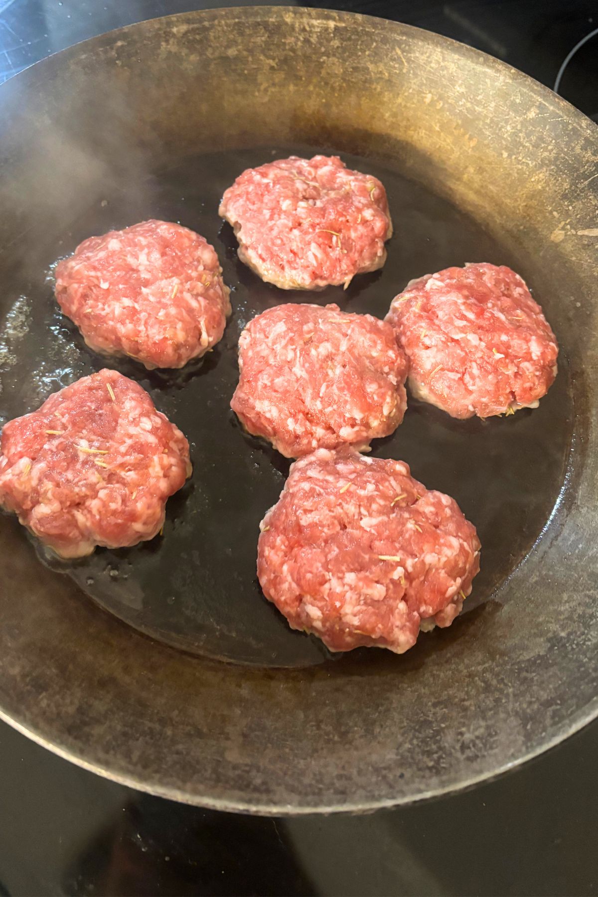 six homemade pork breakfast sausage patties frying in a cast iron pan