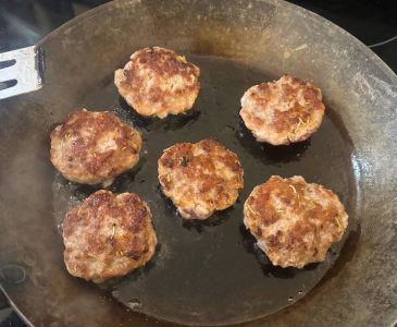six homemade pork breakfast sausage patties being fried in a cast iron pan