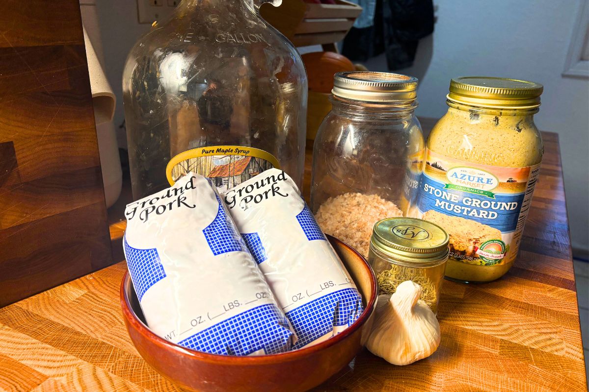 ingredients to make homemade pork breakfast sausage patties including ground pork maple syrup salt mustard rosemary and garlic on a butcher block counter top