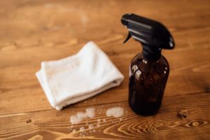 amber spray bottle of non-toxic cleaning solution next to a cotton cloth rag on a wooden surface