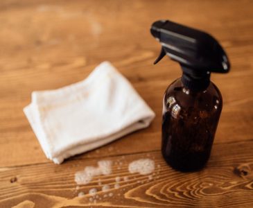 amber spray bottle of non-toxic cleaning solution next to a cotton cloth rag on a wooden surface