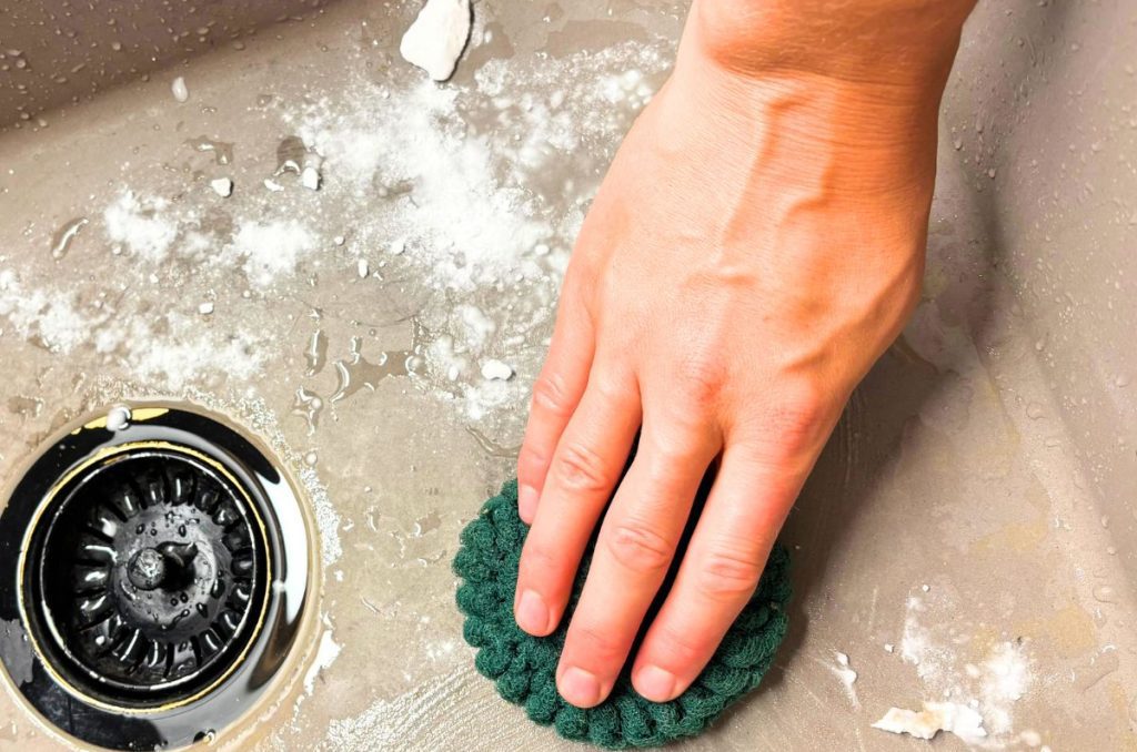 hand using a green sponge to clean a gray sink with baking soda