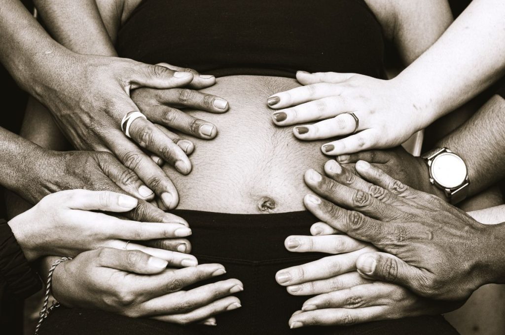 multiple hands laying over a pregnant women's stomach blessing her fertility