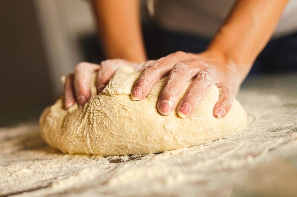 woman working rhythmically in kitchen kneading bread dough with hands