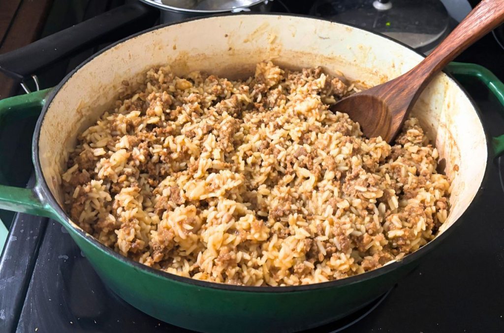 large portion of the best easy pad Thai in a green dutch oven with a wooden spoon on the stove top