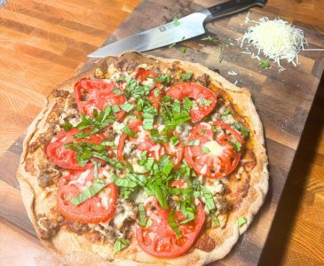 homemade pizza with tomato, basil, and sausage on a wooden cutting board with a knife and cheese made without meal planning