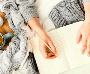 woman settled into the rhythm of writing in a journal while sitting under a blanket with a cup of tea