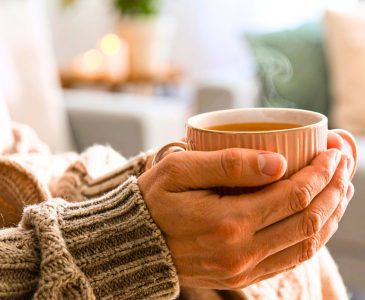 woman practicing slow living by leisurely holding a warm cup of tea in her hands