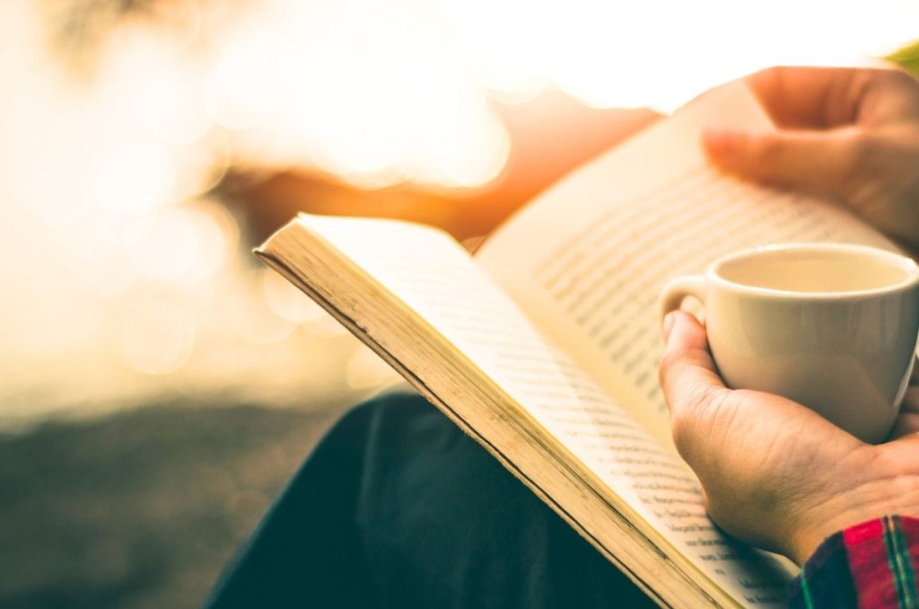 woman reading a book outside with a cup of coffee practicing slow living