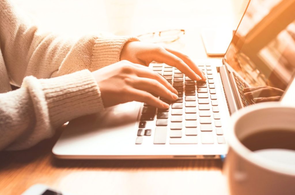 woman typing on a laptop with her glasses and a cup of coffee nearby
