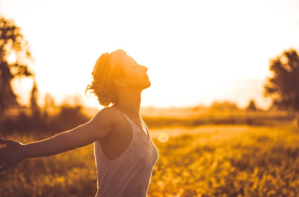 woman practicing slow living by taking a walk with her arms outstretched in a meadow