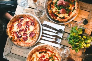3 handmade pizzas made with slow food principles on a wooden table with cups, silverware and napkins