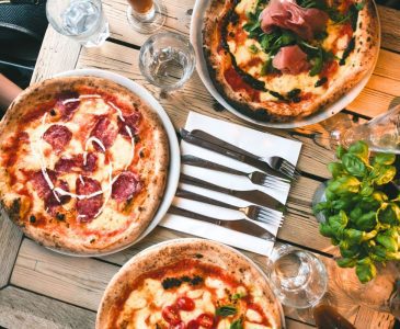 3 handmade pizzas made with slow food principles on a wooden table with cups, silverware and napkins