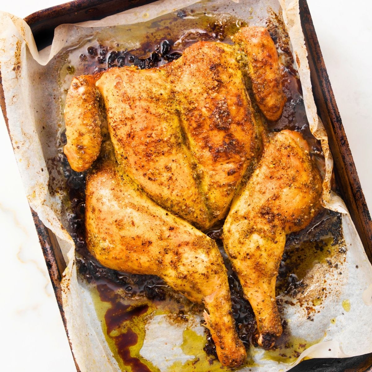whole oven roasted spatchcocked chicken on a baking sheet with parchment paper