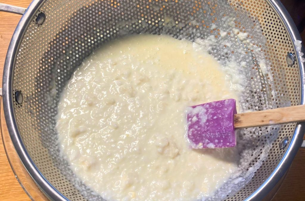 slow fermented kefir being strained through a stainless steel strainer with a spatula in it