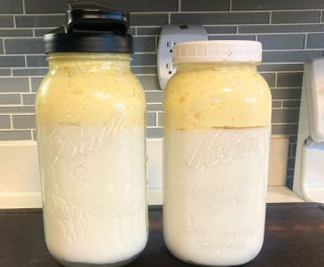 two half gallon mason jars filled with slow fermented kefir in which the cream has risen to the top sitting on a wooden cutting board