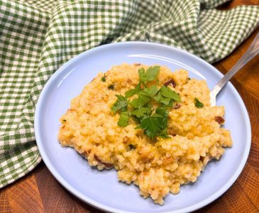 butternut squash risotto with bacon topped with fresh parsley on a blue plate sitting on top of a green gingham towel