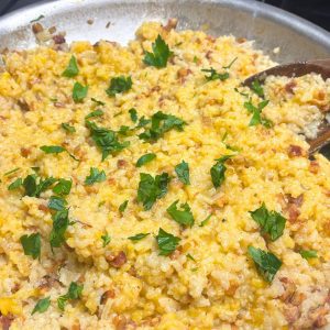 butternut squash risotto with bacon in a pan with a wooden spoon garnished with fresh parsley