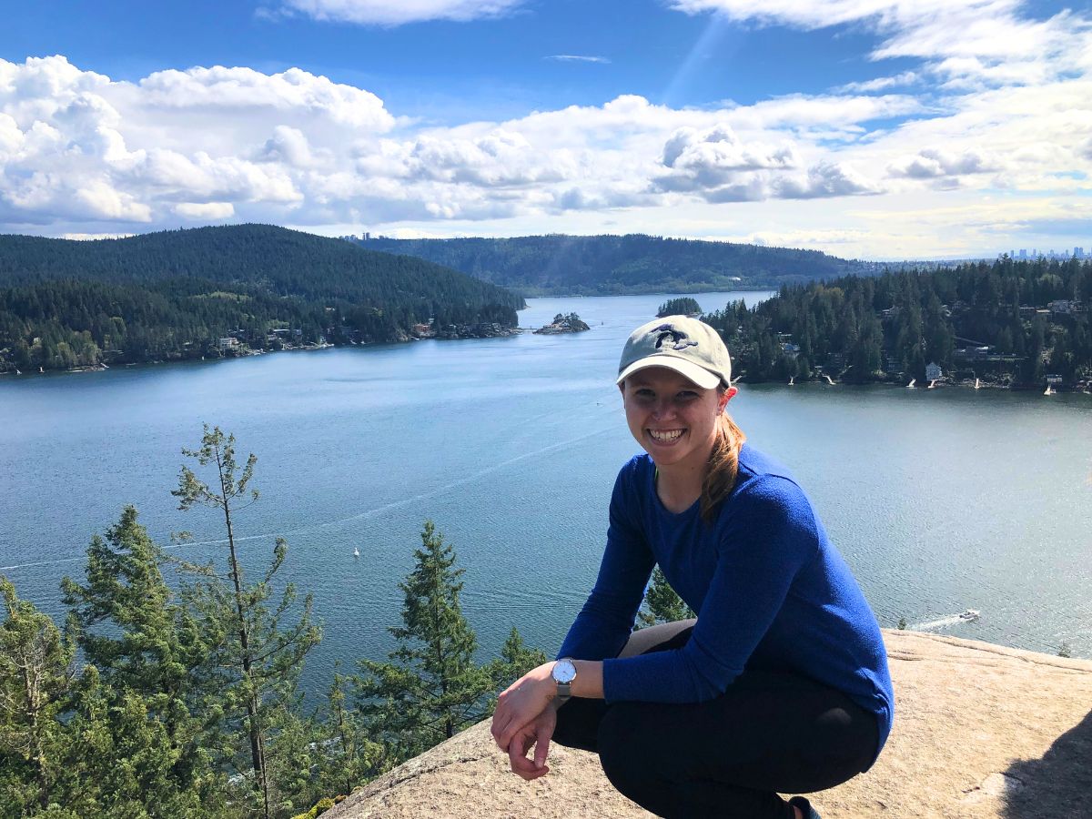 woman sitting on a large rock overlooking a mountainous clear blue lake