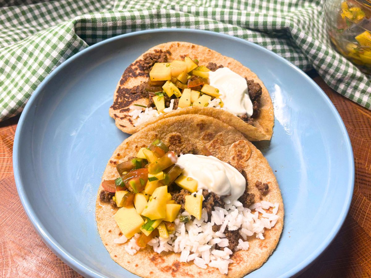 two tacos made with homemade flour tortillas topped with rice salsa and sour cream on a blue plate