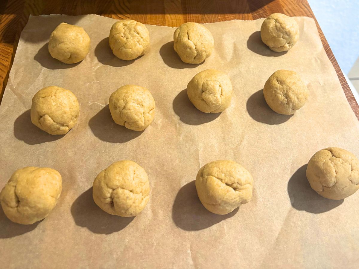 twelve balls of homemade flour tortilla dough on a piece of parchment paper