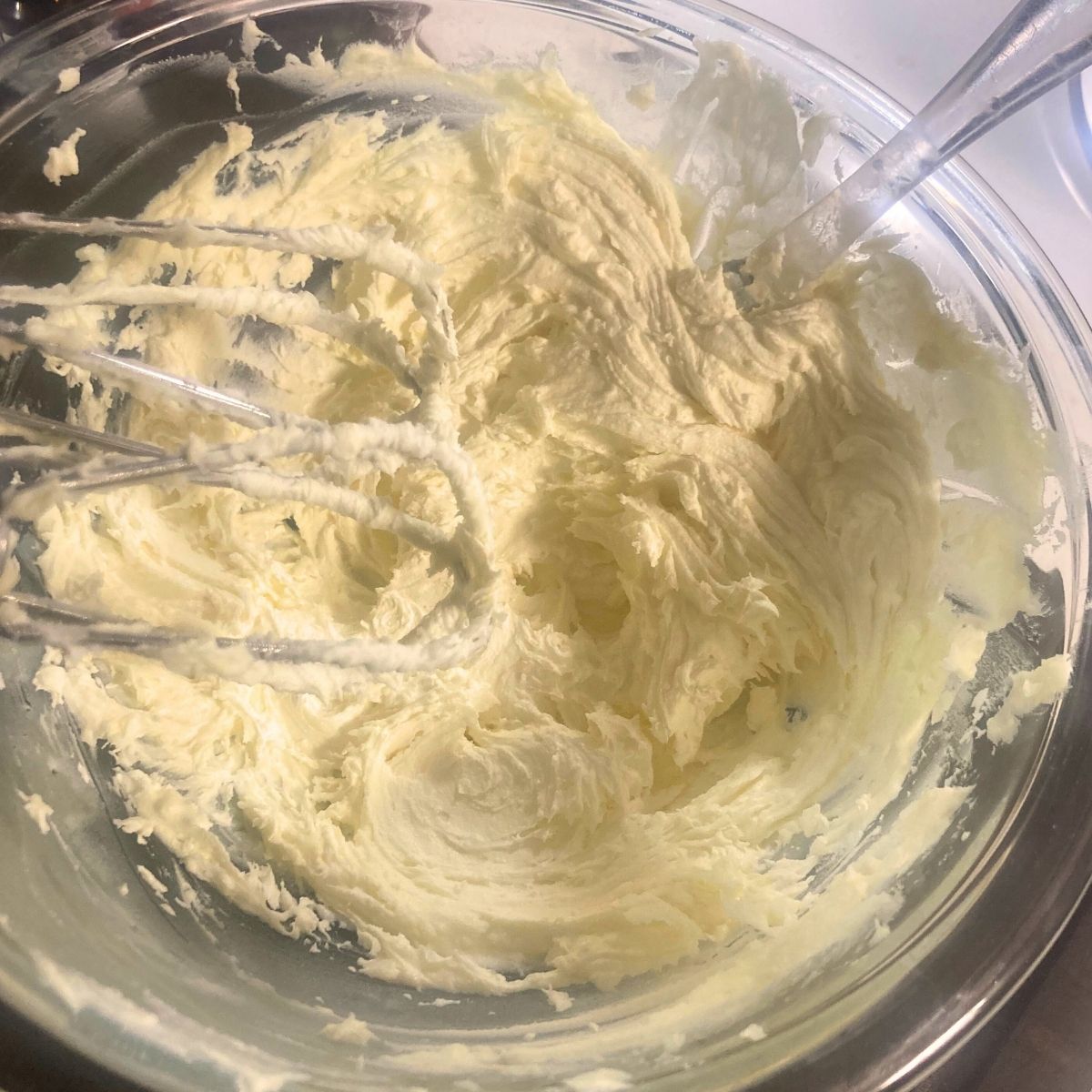 Whipped tallow body butter lotion in a glass bowl with a hand mixer whipping the lotion