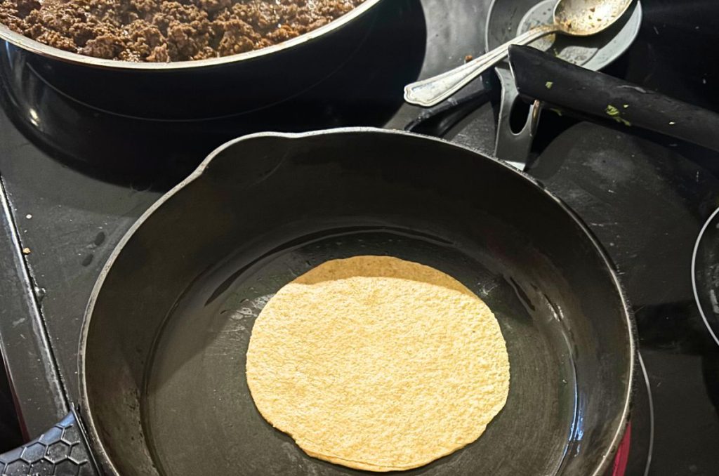 homemade flour tortilla cooking in a cast iron pan on an electric stove top