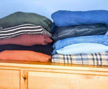 two stacks of clothing for a ten item capsule wardrobe folded neatly on top of a wooden dresser