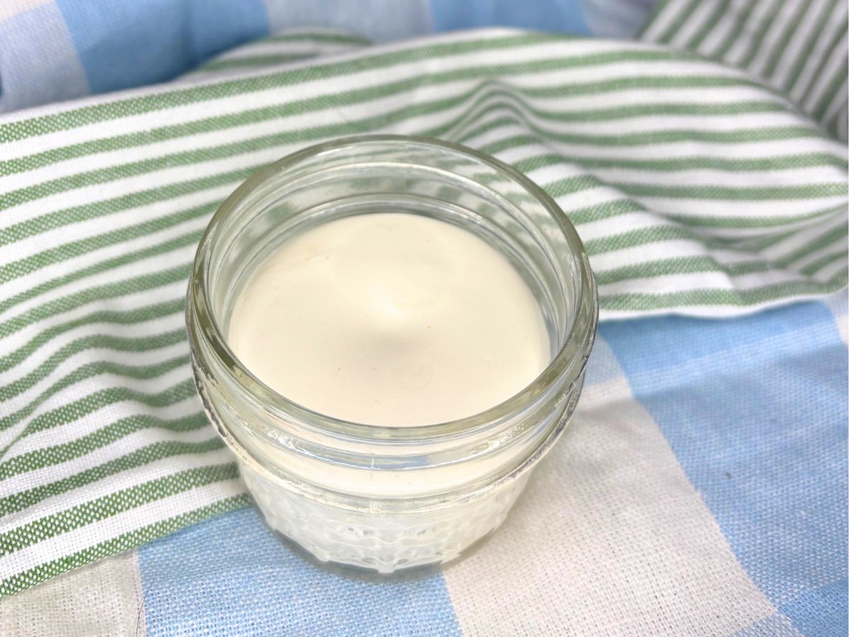 homemade non-toxic beef tallow sunscreen in a two ounce mason jar sitting on top of green, blue, and white towels