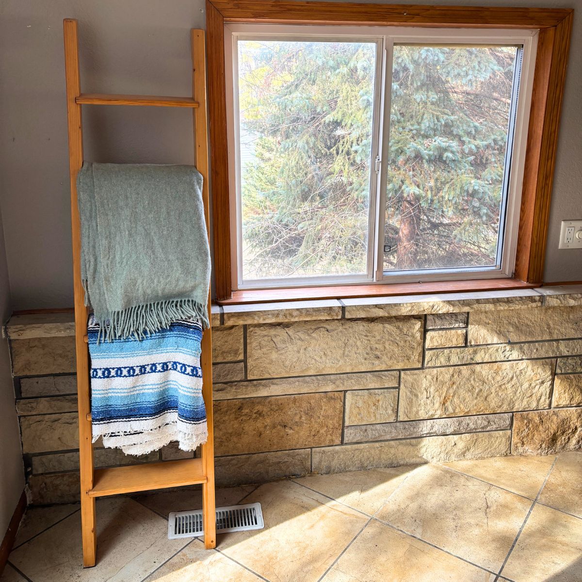 minimalist home displaying blanket ladder with two blankets next to a window located above a limestone wall