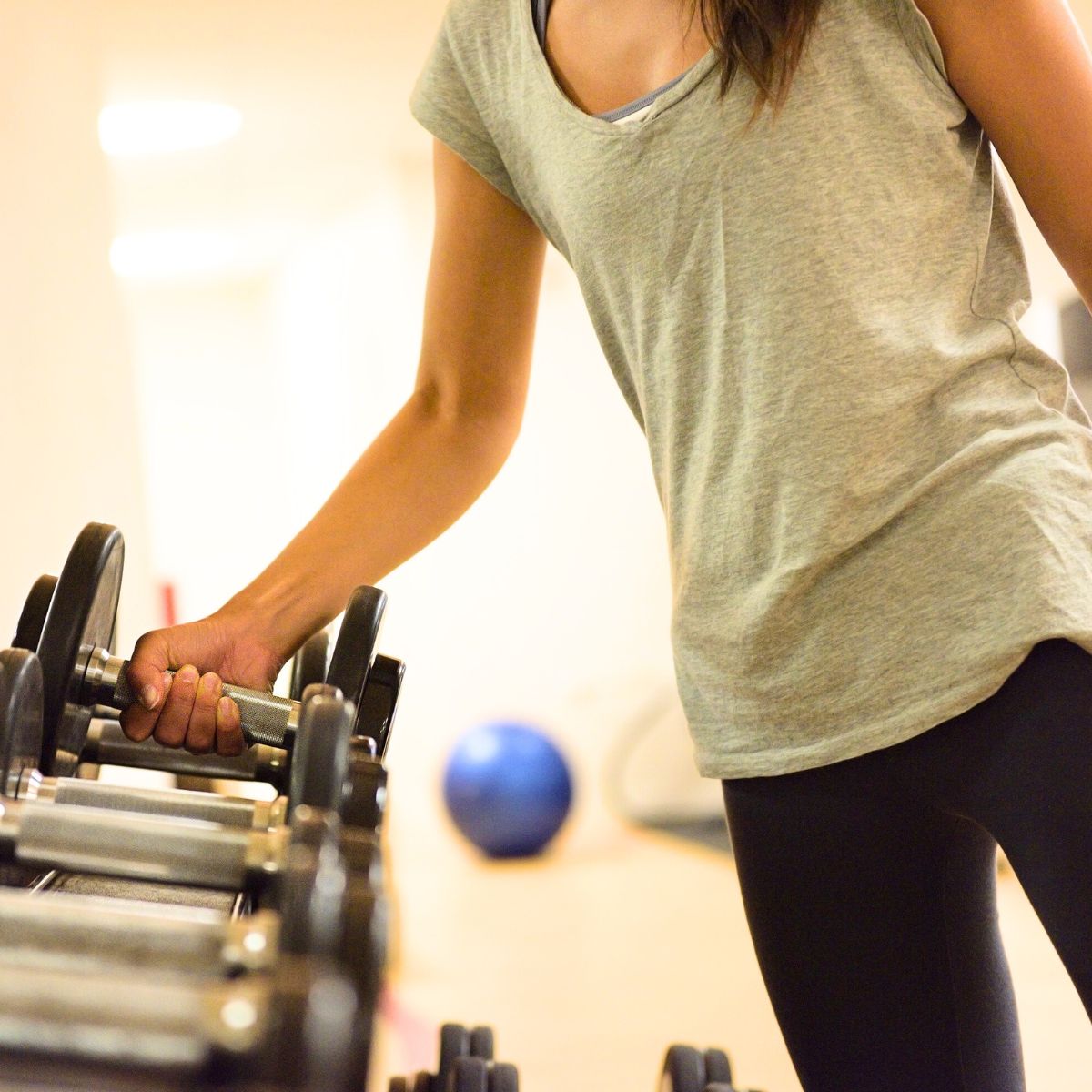 woman wearing a short sleeve grey shirt grabbing a dumbbell off of a rack of weights