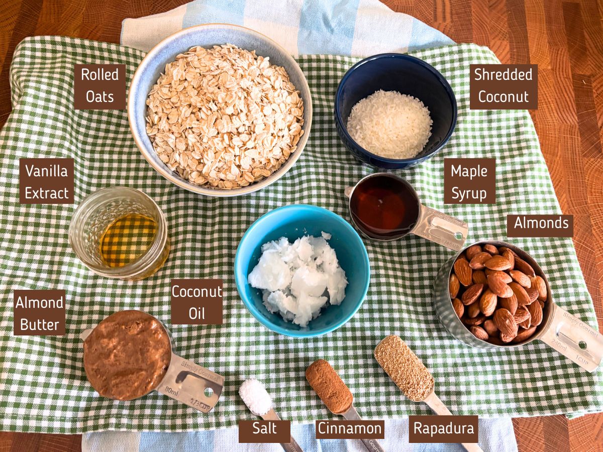 ingredients for a making homemade cinnamon roll granola recipe including rolled oats vanilla extract shredded coconut maple syrup almonds coconut oil almond butter salt cinnamon and rapadura