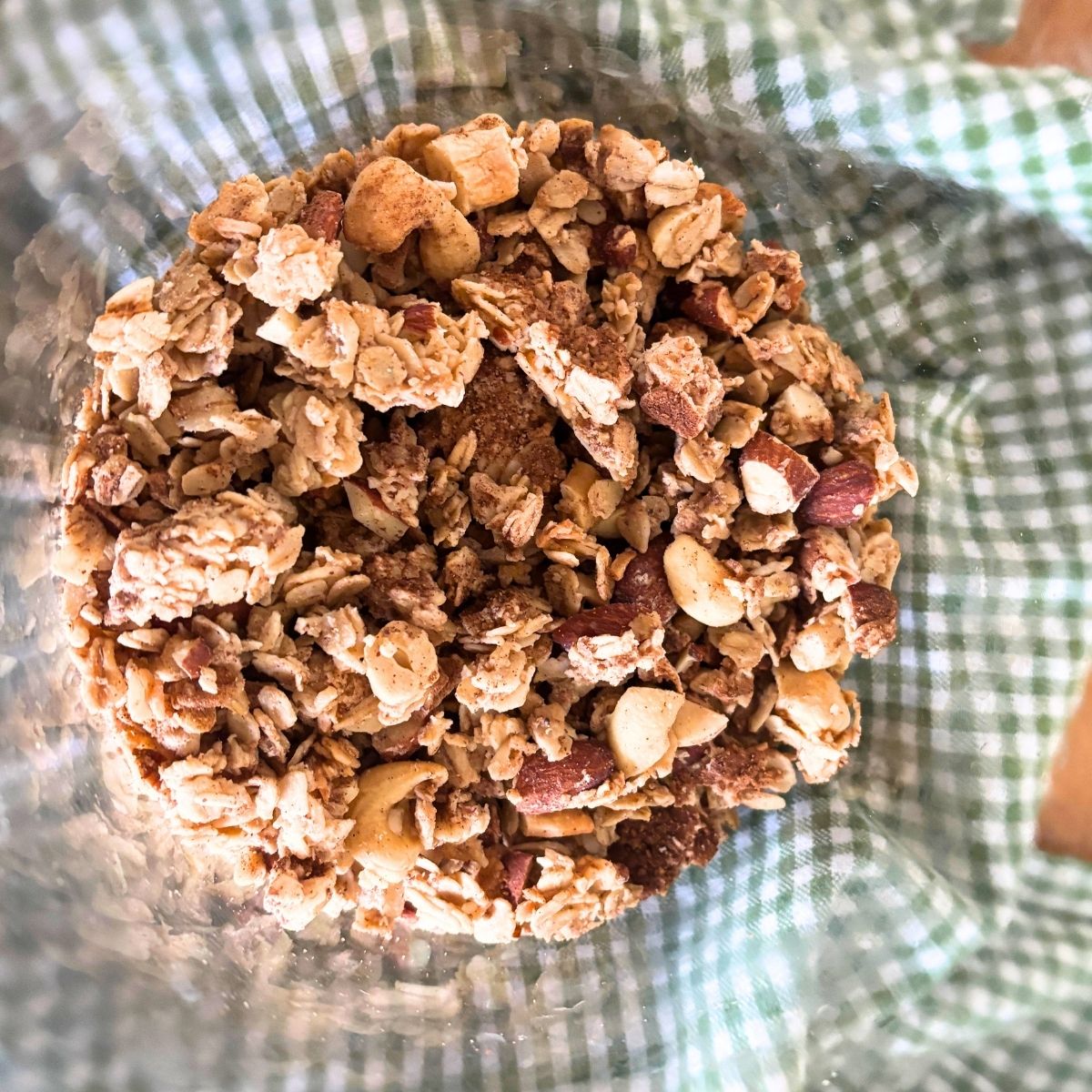homemade cinnamon roll granola in a glass jar sitting on top of a green checked tea towel