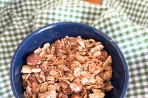 navy blue bowl filled with homemade cinnamon roll granola sitting on a green checked towel