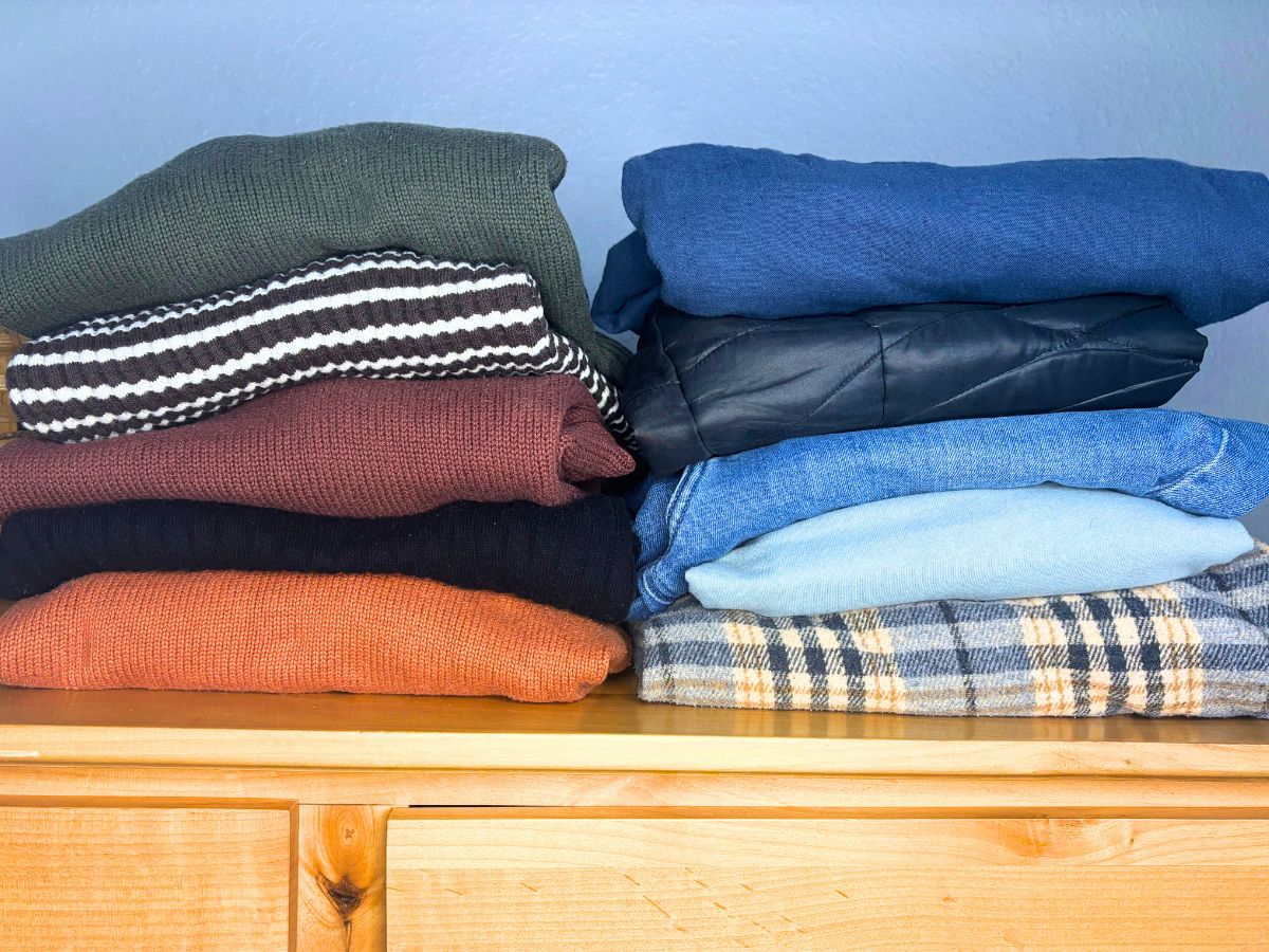 10 item capsule wardrobe folded and stacked on top of a wooden dresser