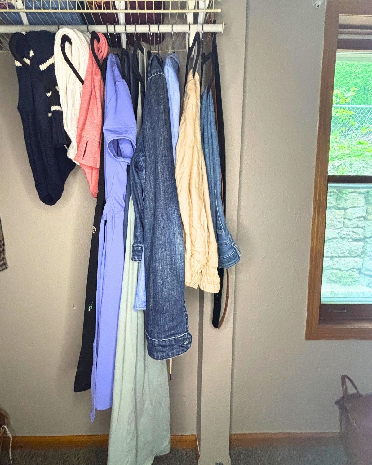10 item capsule wardrobe hanging in a closet next to a window