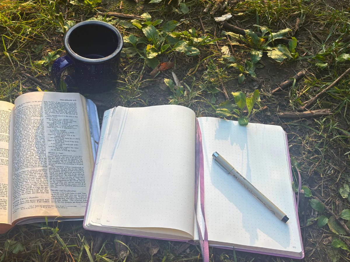 open notebook and pen next to a cup of coffee and bible in the grass