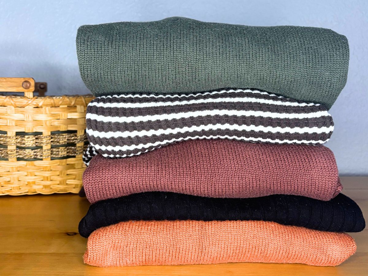 sweaters folded on top of a wooden dresser next to a wicker basket